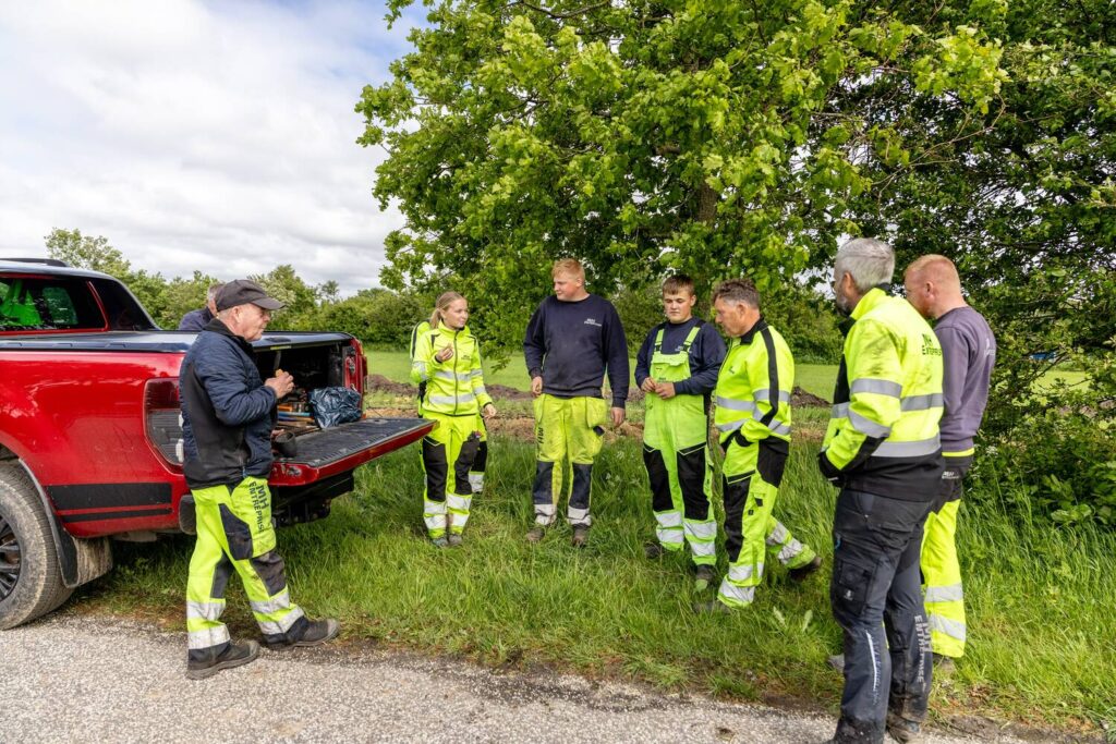 Arbejdere i sikkerhedstøj samles ved rød pickup på landet
