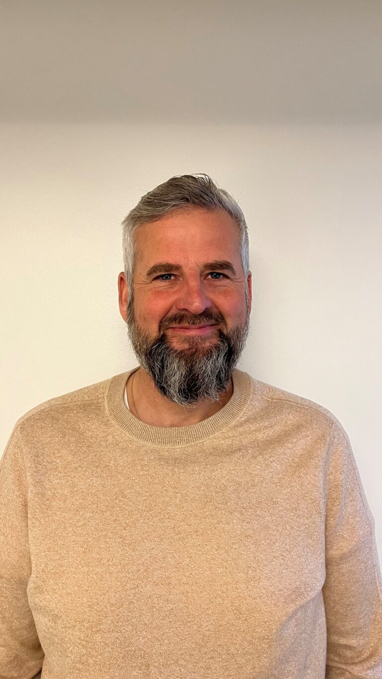 Mand med gråt skæg og beige sweater smiler