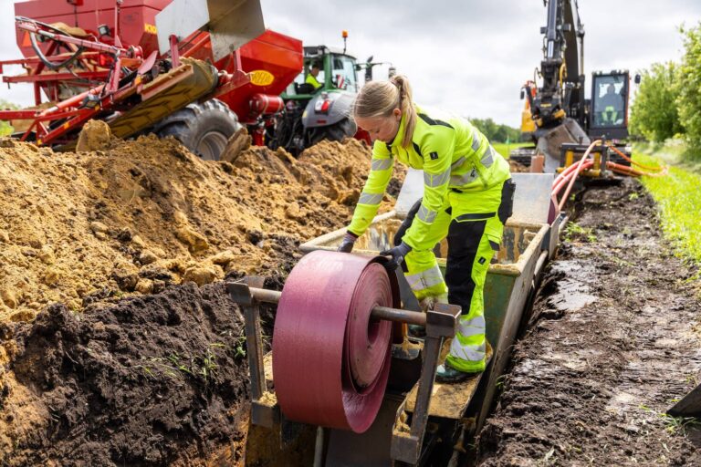 Arbejder lægger kabel i udgravet rende med entreprenørmaskiner